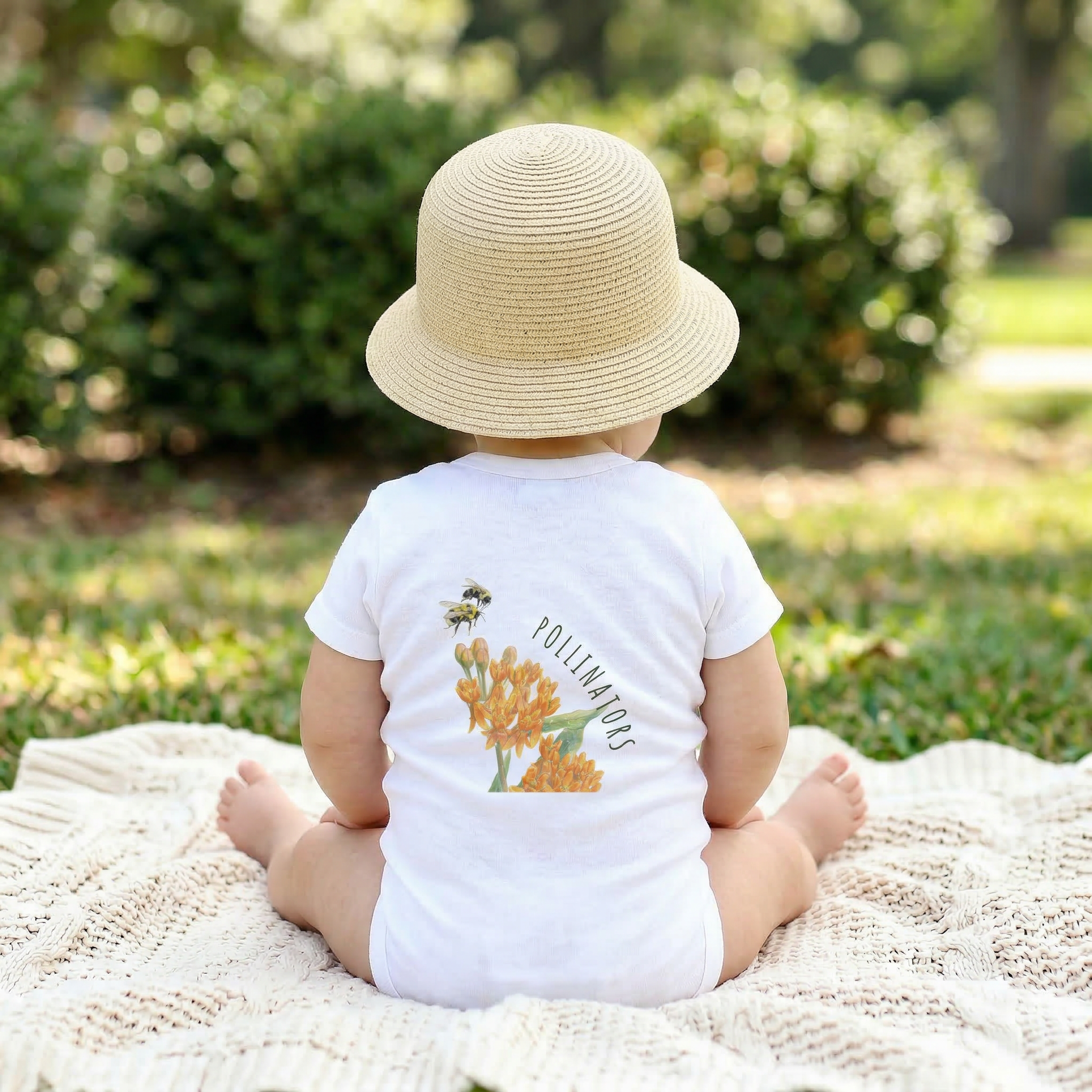 Backview of Baby sitting on a blanket wearing a White 100% cotton baby one-piece featuring the bumblebee design from the Golden Dust collection.