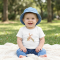 Baby sitting on a blanket outdoors wearing a blue hat and"Sweet Nectar hummingbird illustration on a white Bella + Canvas baby short sleeve tee."