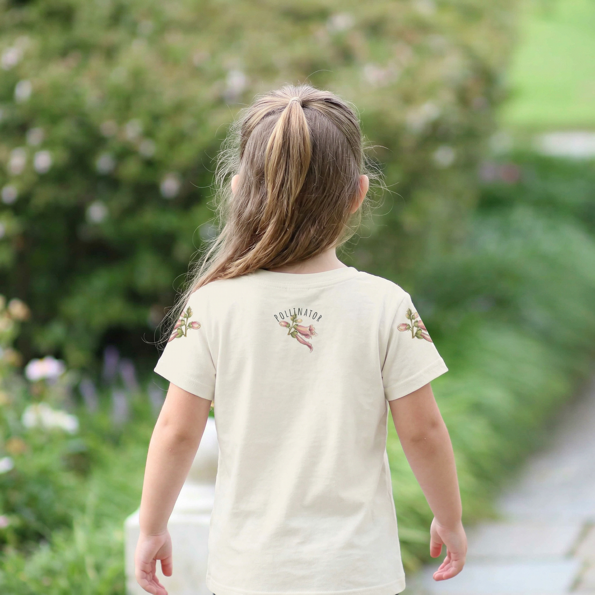 Back view of a Child wearing a cream t-shirt with floral designs in a garden setting