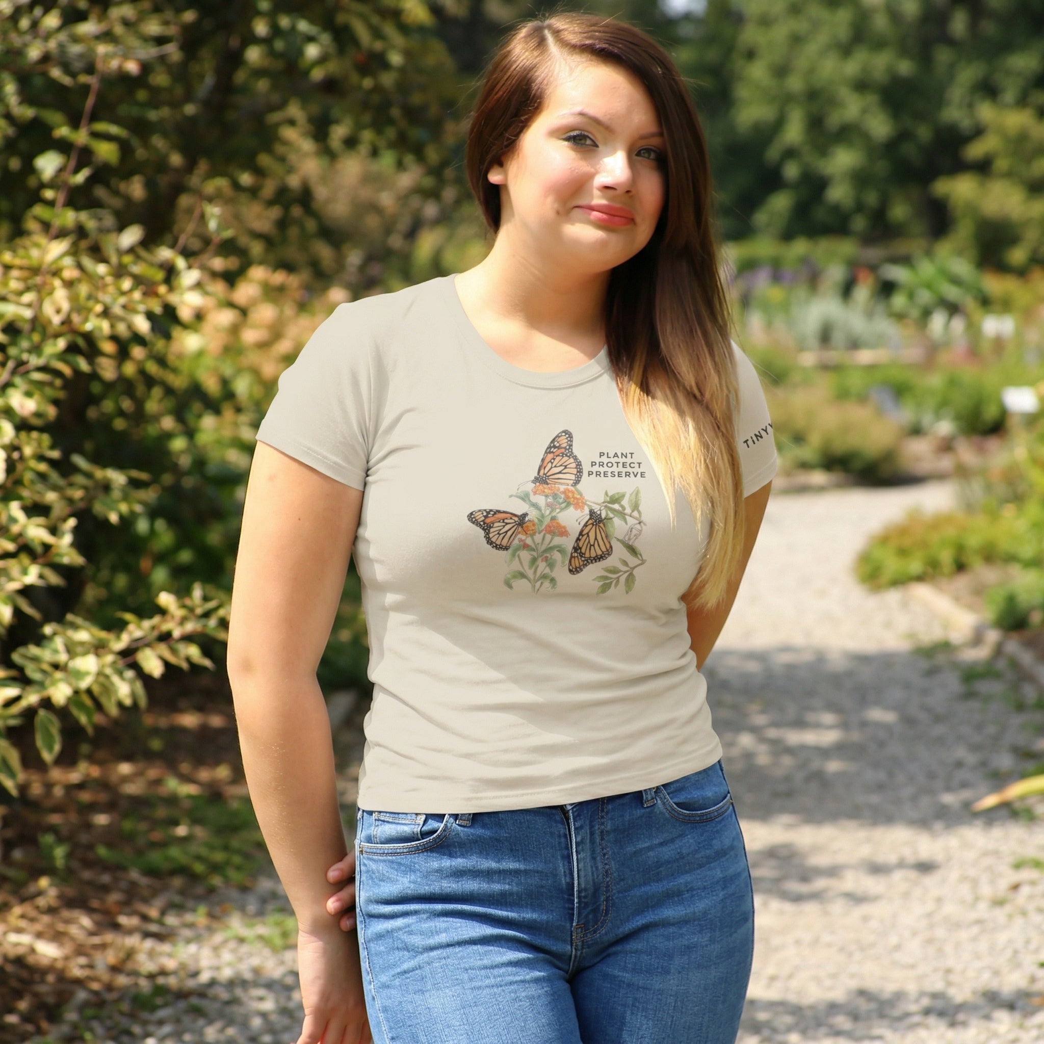 Woman wearing a t-shirt with butterfly design in a garden setting. Tinywing Tales