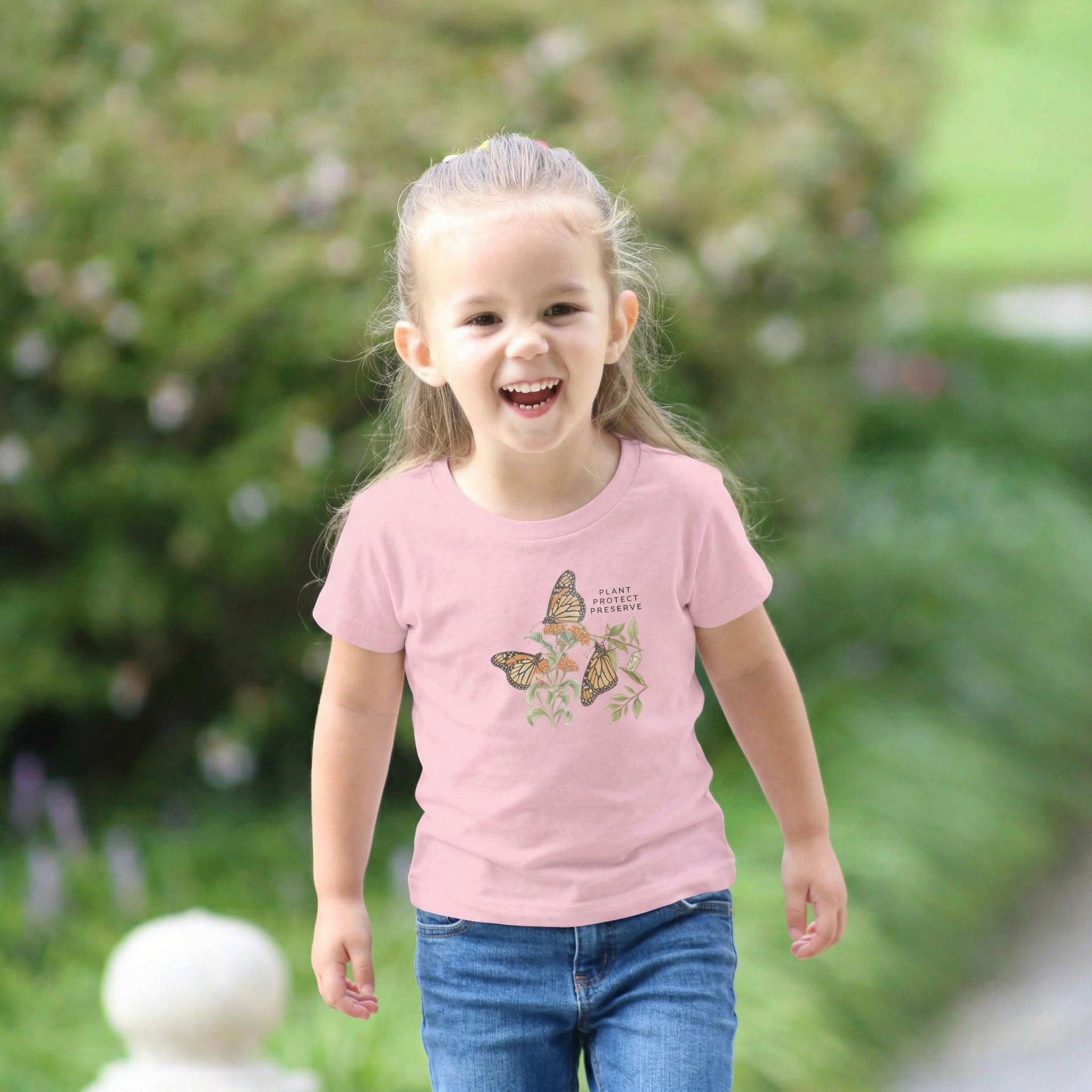 Child wearing a pink t-shirt with butterfly design outdoors. Tinywing Tales