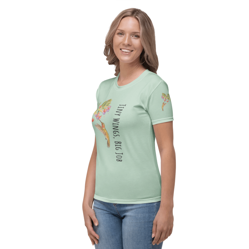 left side view of Woman wearing a light green t-shirt with a graphic design of a hummingbird and flowers and text "Tiny Wings, Big Job" 