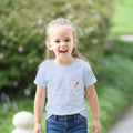 Child wearing a light blue t-shirt with a small design bee and flower on a blurred green outdoor background