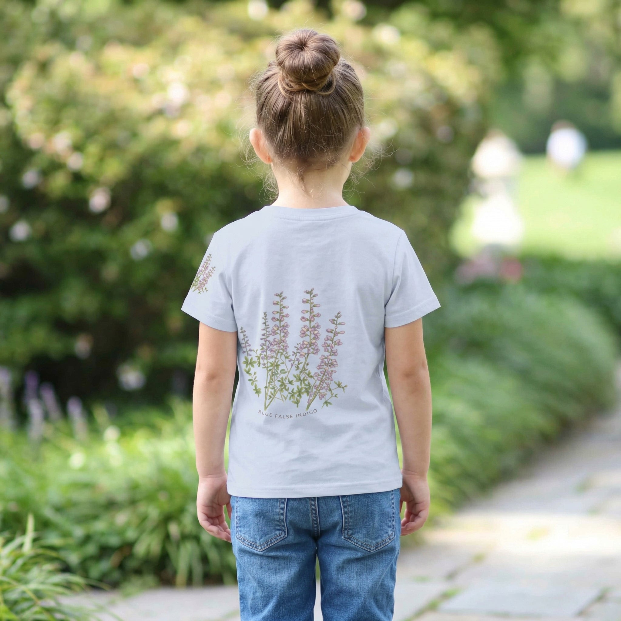 Backview of Child wearing a light blue t-shirt with a small design bee and flower on a blurred green outdoor background