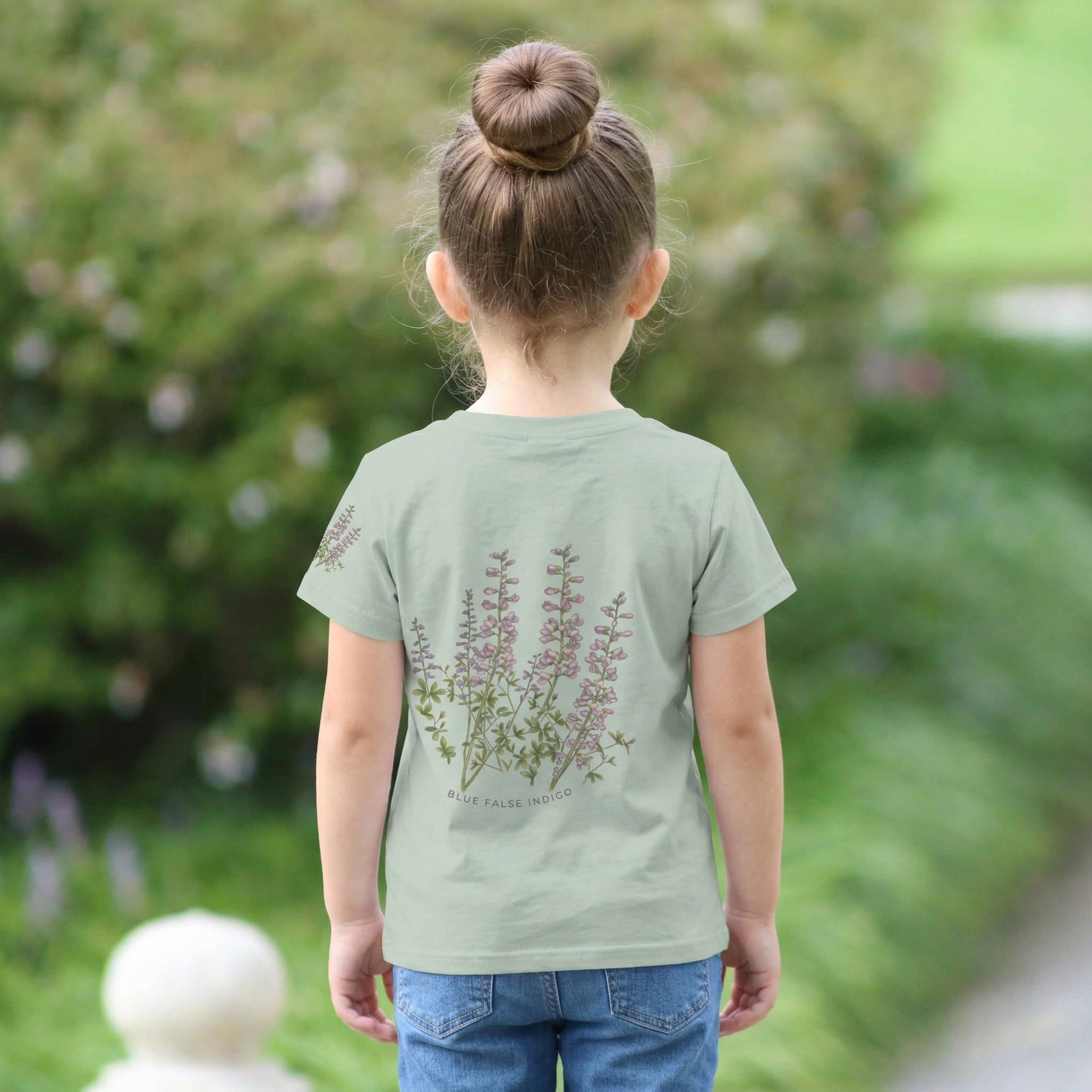 Backview of a Child wearing a light sage t-shirt with a small design on a faux pocket design of a bee and flower. Text "Bloom Bound" Tinywing Tales