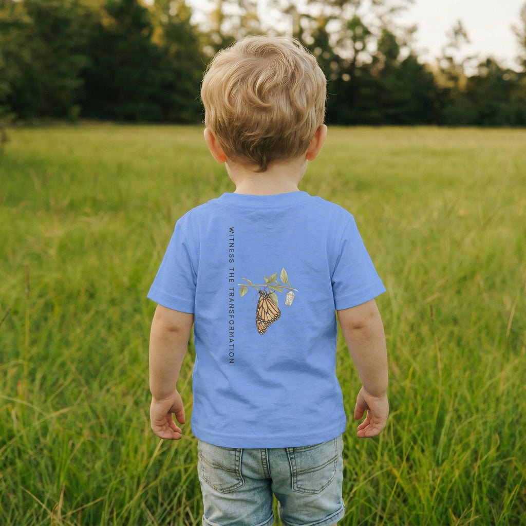 Back view of a Child wearing a blue t-shirt with a butterfly design in a grassy field
