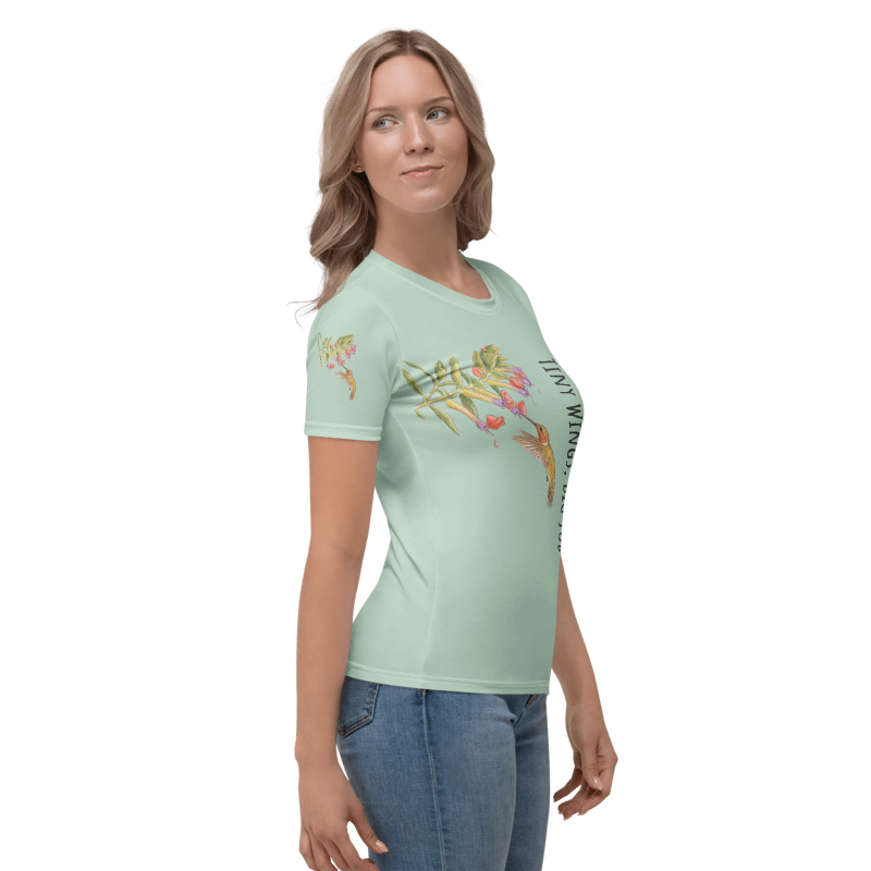 right side view of Woman wearing a light green t-shirt with a graphic design of a hummingbird and flowers and text "Tiny Wings, Big Job" 