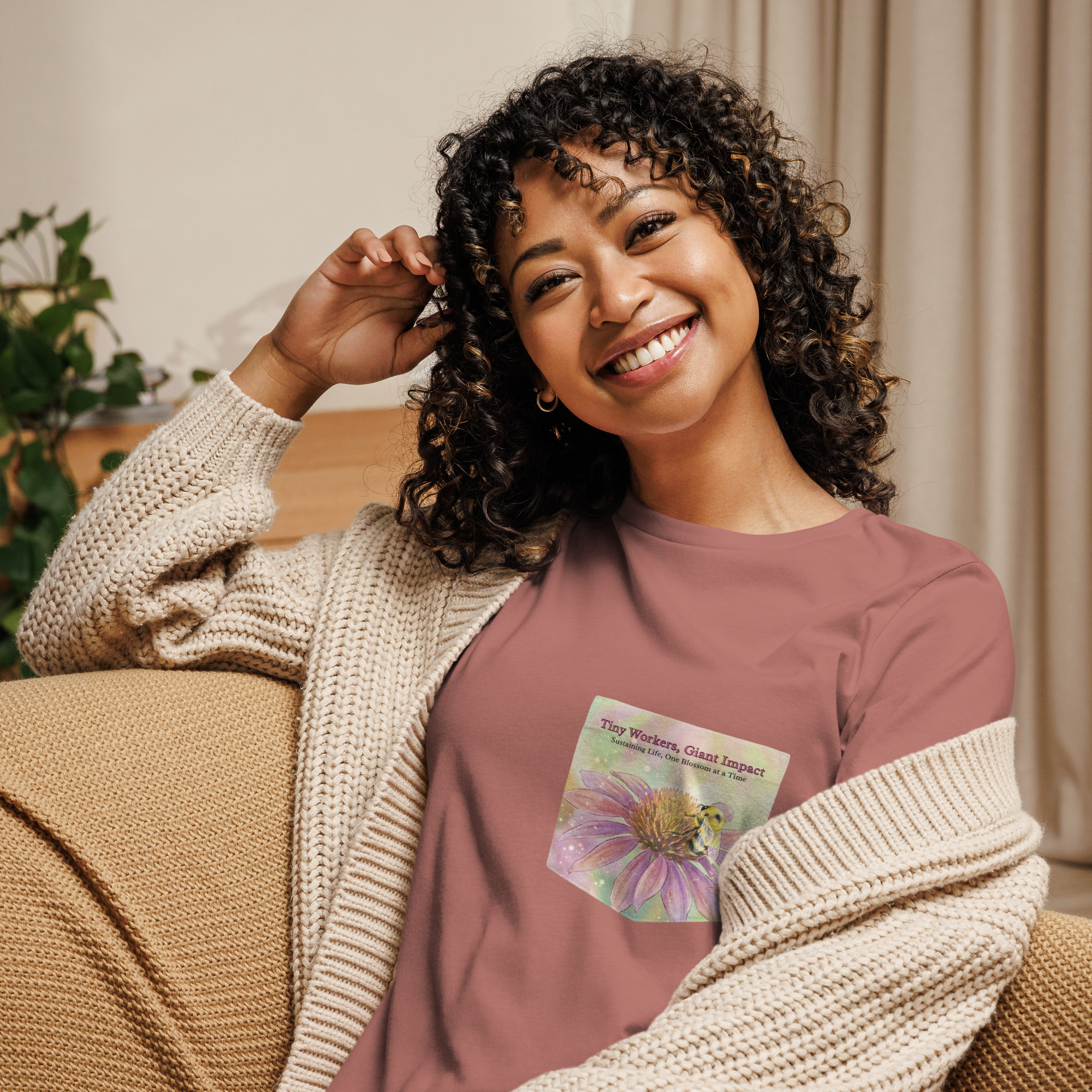 Woman wearing a mauve faux pocket tee with a nature-themed design, bee and condflower sitting on a couch.