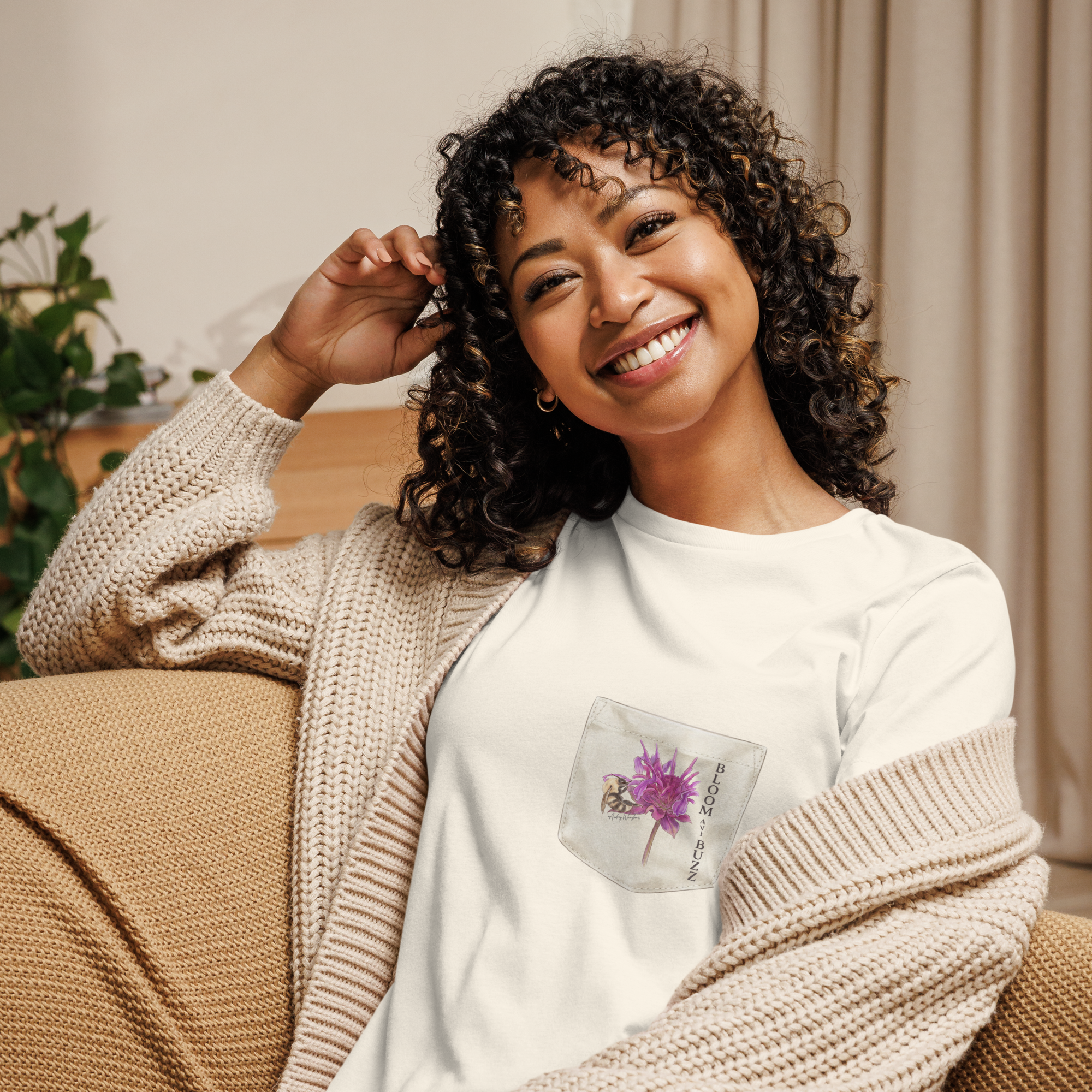 Woman wearing a beige t-shirt with bee and flower and text,  "BLOOM AND BUZZ"